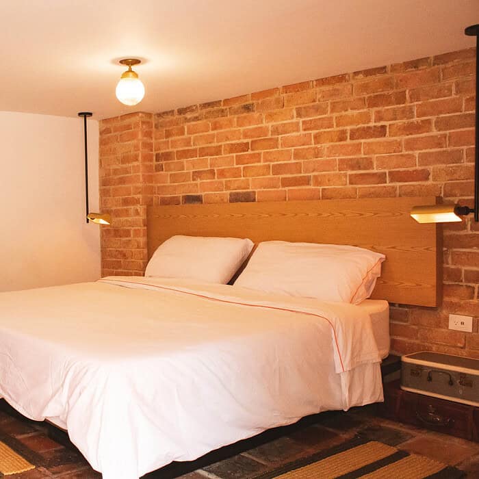 Hotel boutique con cama doble, paredes de ladrillo y decoración moderna en el interior de un hostal Masaya.