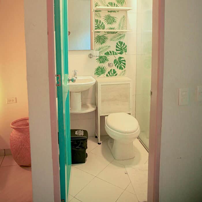 Lavabo y paredes decoradas con hojas verdes, baño acogedor en un hostal boutique de Masaya, Colombia, con iluminación suave y ambiente natural, ideal para una estancia cómoda y relajante.