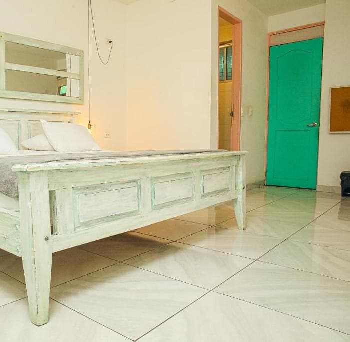 Cama de madera envejecida en habitación de hotel boutique con paredes blancas y suelo de baldosas.