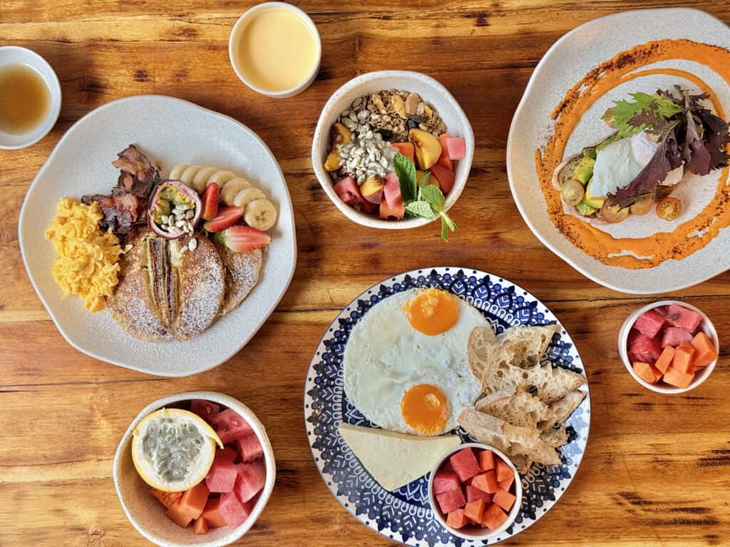Desayuno variado con huevos, fruta fresca, pan y bebidas calientes en un ambiente acogedor.