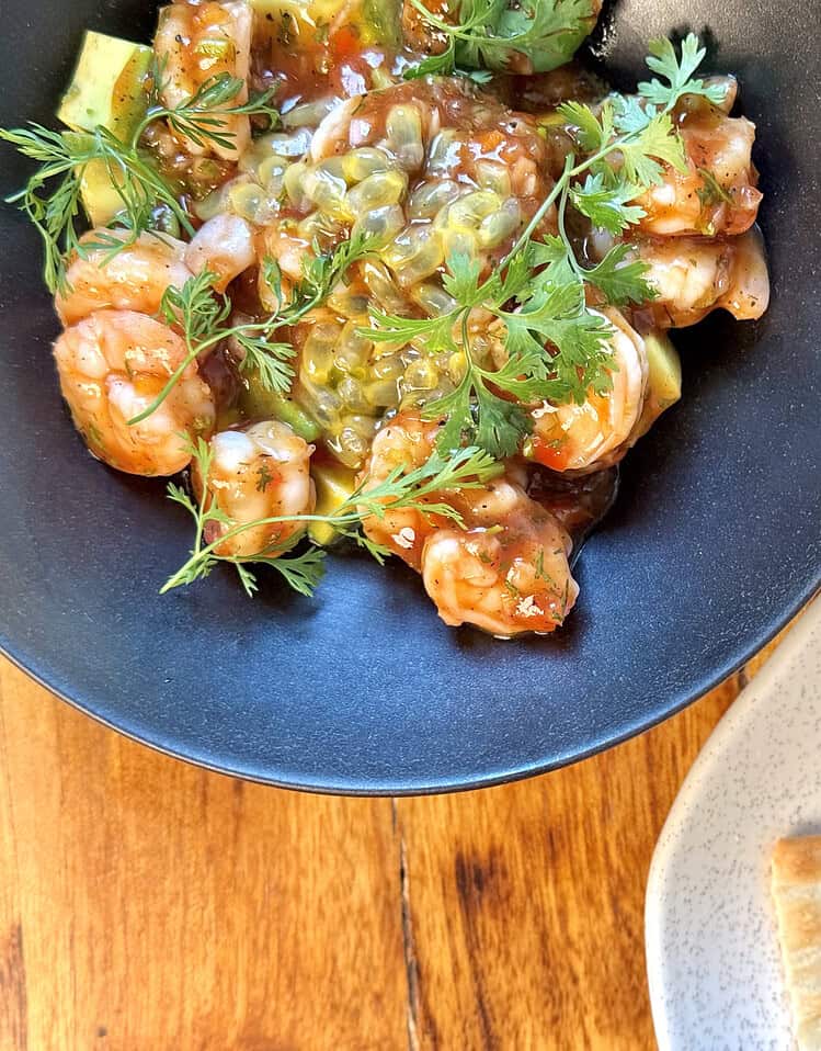Shrimp ceviche con cilantro y salsa en plato negro, acompañado de crispetas en plato blanco, en ambiente acogedor de Masaya.