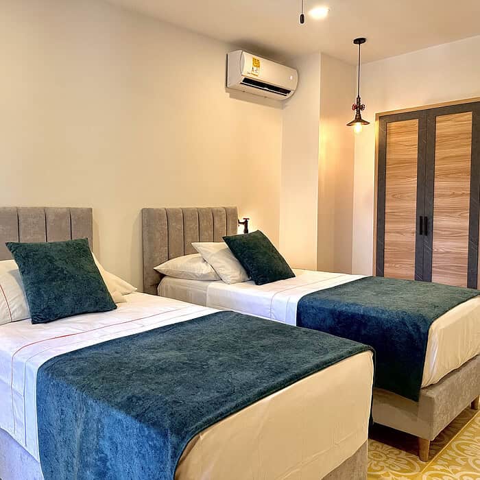 Habitación doble con dos camas, cabeceras acolchadas y ropa de cama blanca, decorada con cojines verdes. Espacio luminoso y moderno, ideal para una estancia confortable en Masaya.