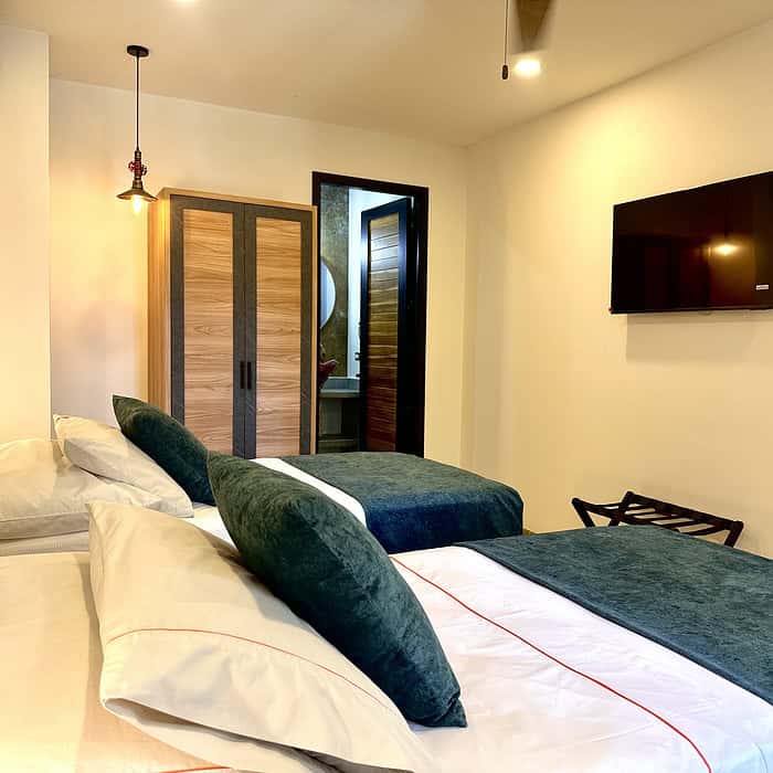 Amplia habitación con cama doble, televisor de pantalla plana y decoración moderna en tonos neutros y verdes. Ideal para una estancia cómoda y relajante en Masaya Experience.