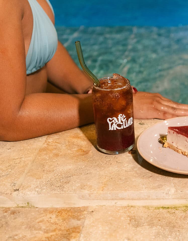 Una tarta de queso con cobertura de frambuesa en una mesa junto a la piscina, acompañada de una bebida fría en un ambiente relajante y veraniego.