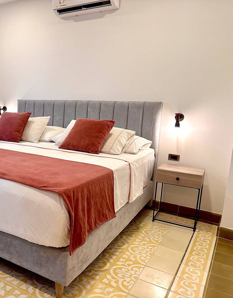 Habitación con cama doble, cabecera acolchada y ropa de cama en tonos terracota y beige, en un ambiente luminoso y elegante, ideal para una estancia confortable en un hotel boutique.