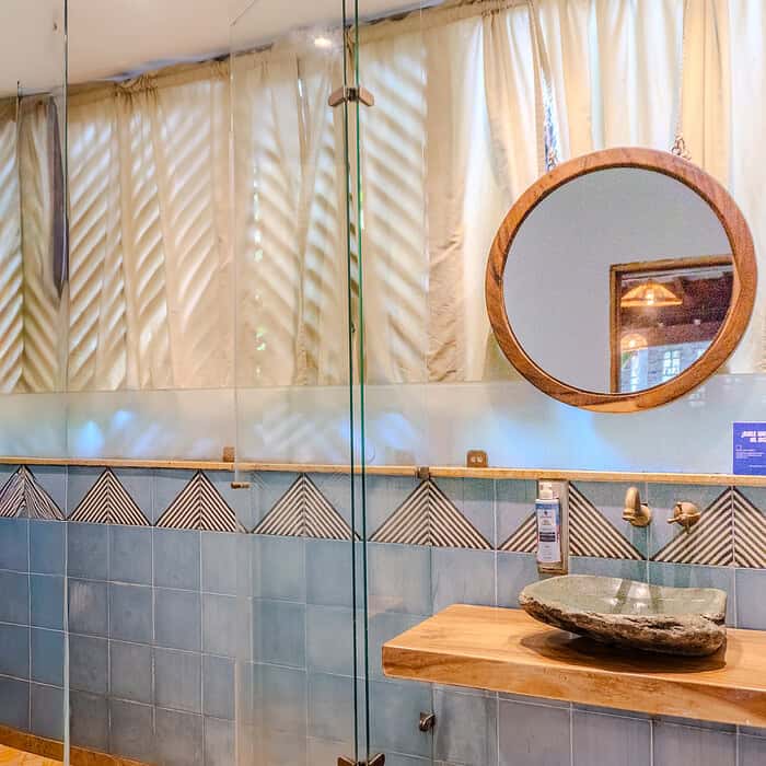 Baño moderno con ducha de vidrio, espejo redondo y detalles en madera en un ambiente luminoso y acogedor.