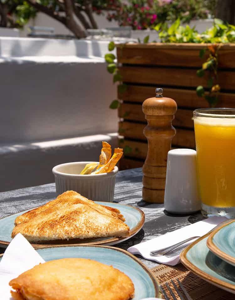 Desayuno al aire libre con huevos revueltos, pan tostado y jugo de naranja en un ambiente soleado.