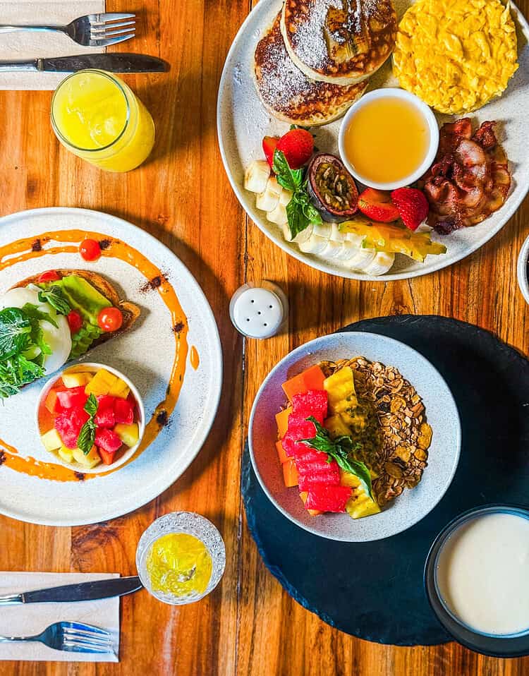 Desayuno con panqueques, frutas, jugo y otros alimentos en un ambiente acogedor.