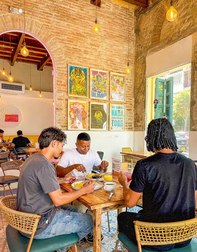 Tres amigos disfrutando desayuno en un restaurante con decoración colorida y ambiente acogedor.
