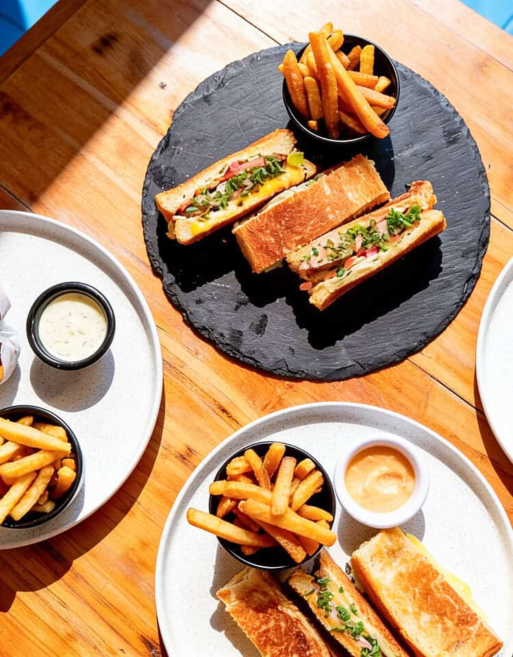 Variedad de sándwiches y papas fritas en diferentes platos en una mesa de madera.