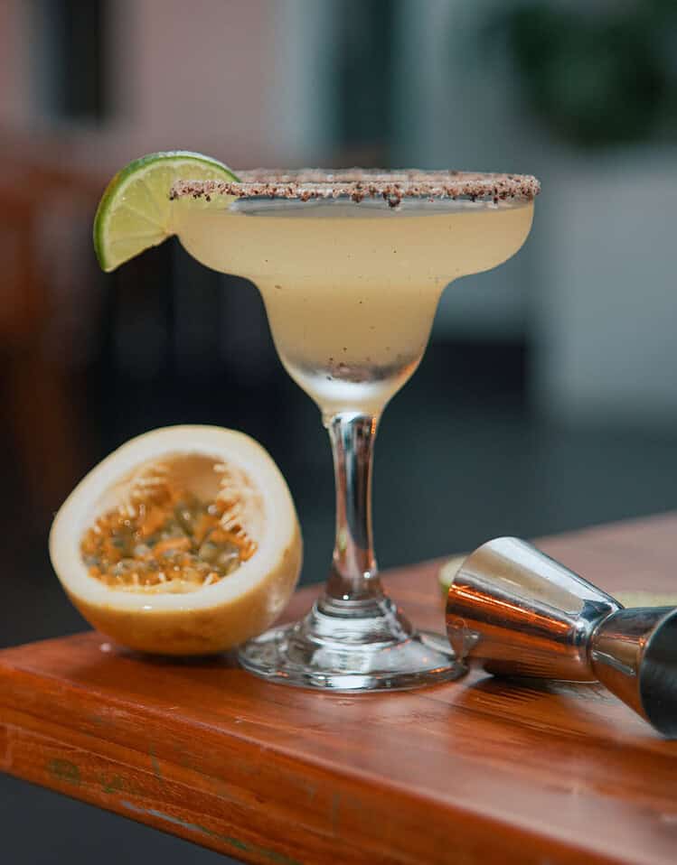 Cóctel en copa con lima, medio limón y coctelera en madera.