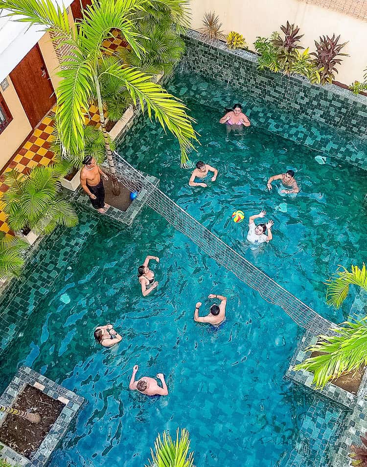 Piscina en un hotel boutique de M con varias personas disfrutando del agua y rodeada de plantas tropicales.