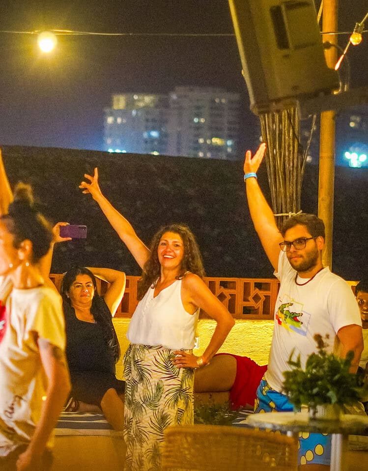 Grupo de personas bailando en una terraza con luces y vista nocturna de fondo.