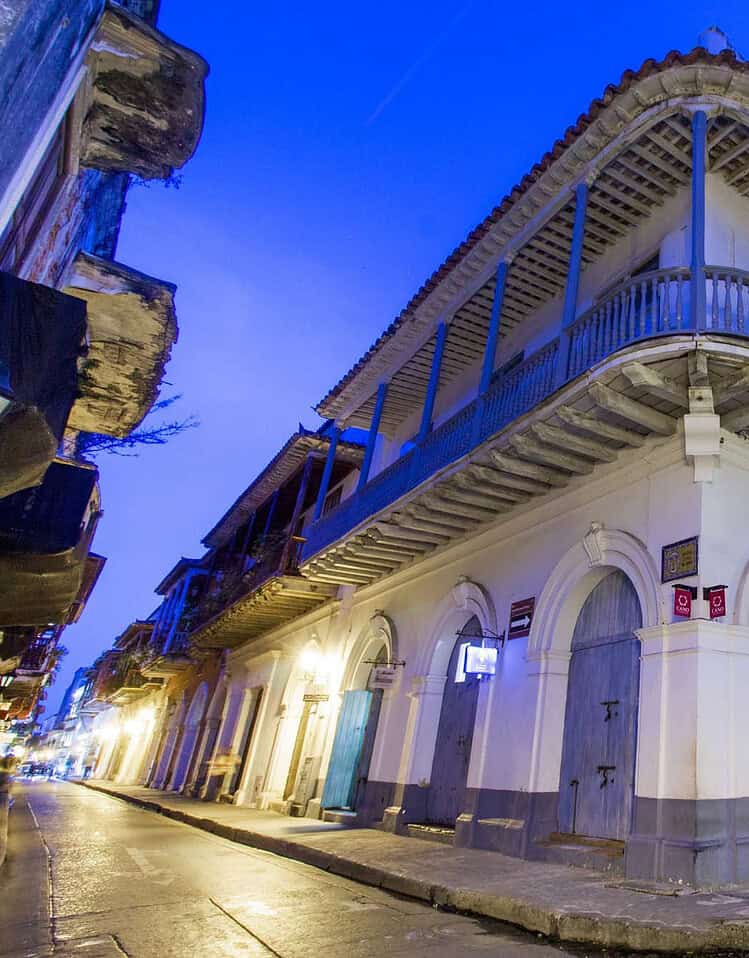 Edificio colonial en una esquina de la calle, con balcones de madera y luces nocturnas.
