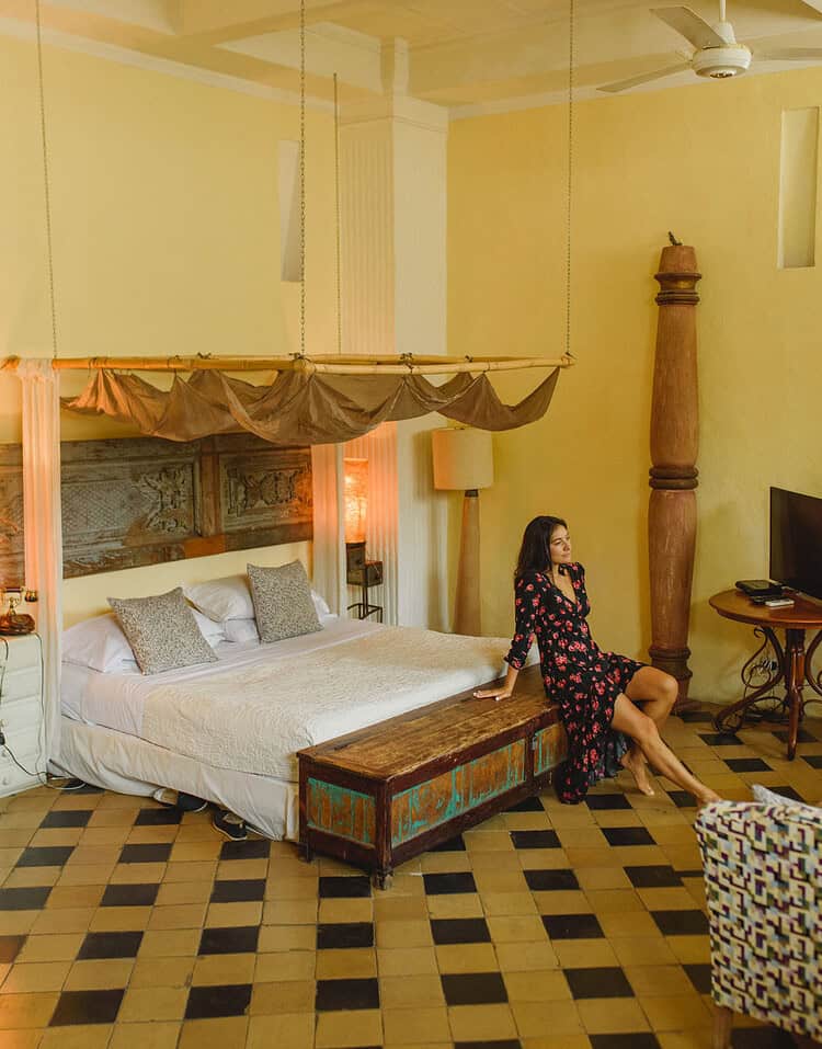 Habitación con cama grande, decoración colonial y mujer sentada en la habitación en M.