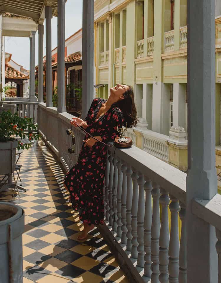 Mujer en un balcón colonial de estilo clásico, disfrutando del sol y la vista en un ambiente tranquilo y elegante.