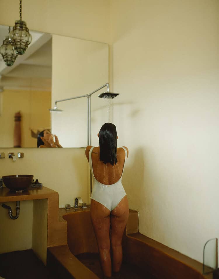 Mujer con cabello largo en ducha del hotel M, vista desde atrás, en un ambiente minimalista y relajante.