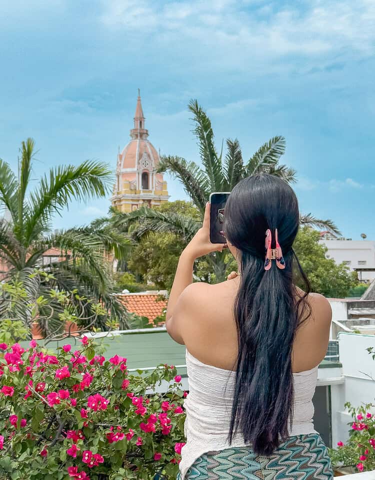 M turista tomando una foto con su teléfono móvil en una terraza con vista a la ciudad y vegetación tropical.