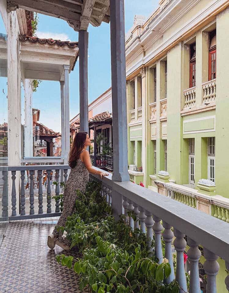 M hotel balcony with a woman looking out over the street and historic buildings in the background.