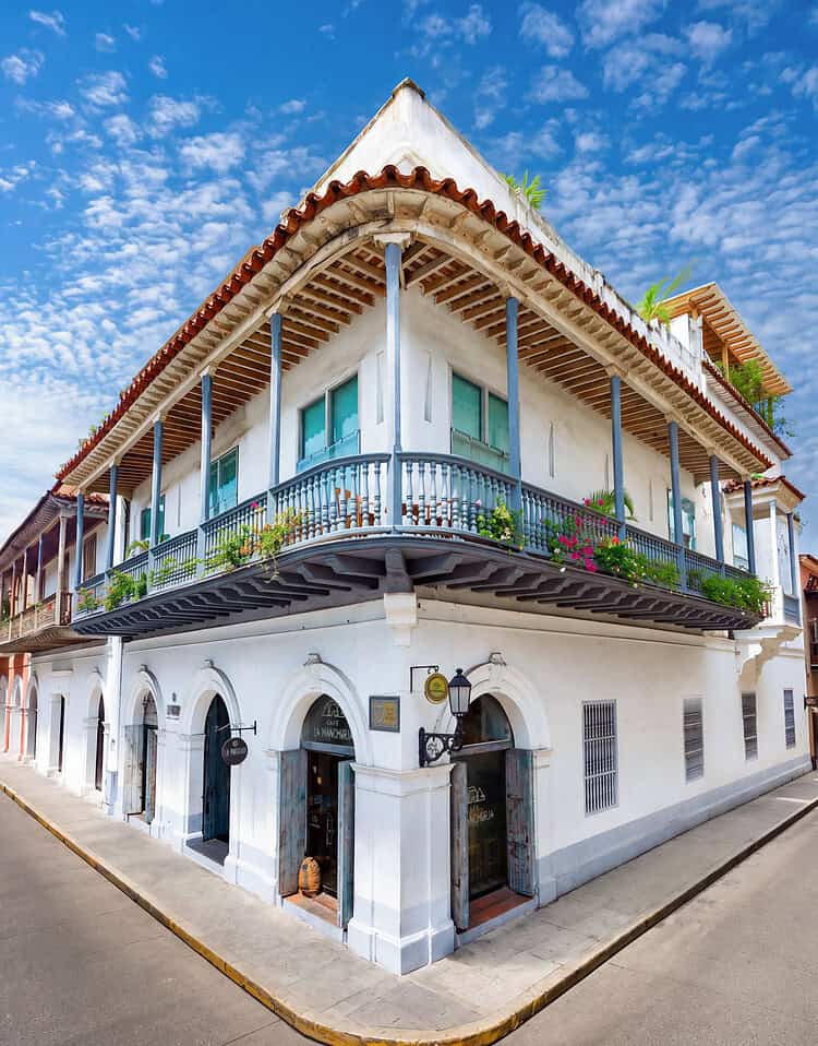 Edificio colonial de dos pisos con balcón y detalles arquitectónicos tradicionales en M, bajo un cielo azul con nubes dispersas.