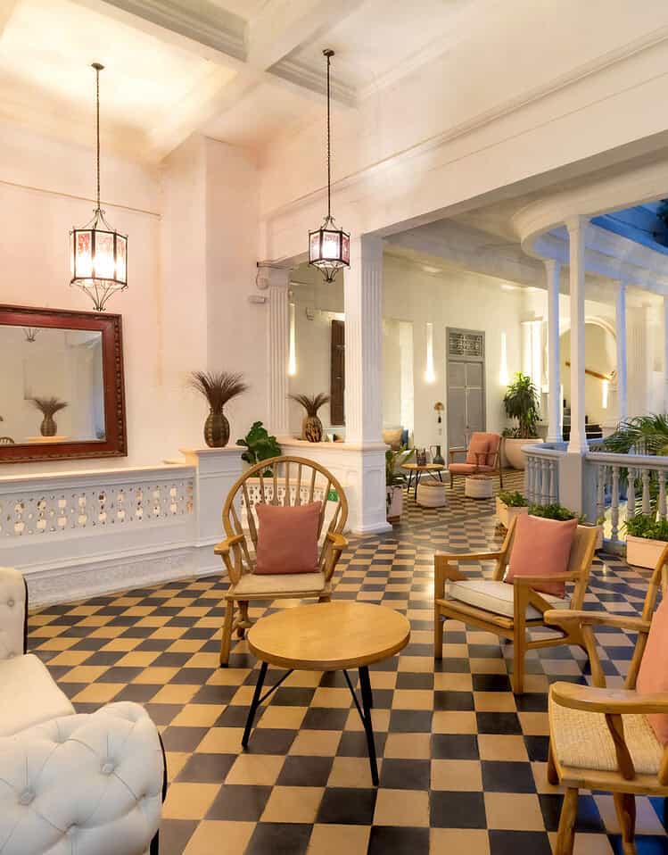 Interior de un hotel boutique con mobiliario clásico, plantas y detalles decorativos elegantes en un ambiente luminoso y acogedor.