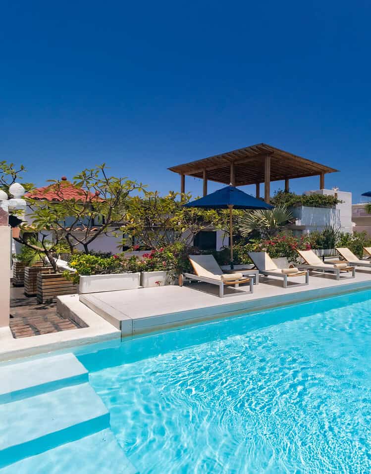 Piscina en hotel M con tumbonas y área de descanso bajo un cielo azul claro.