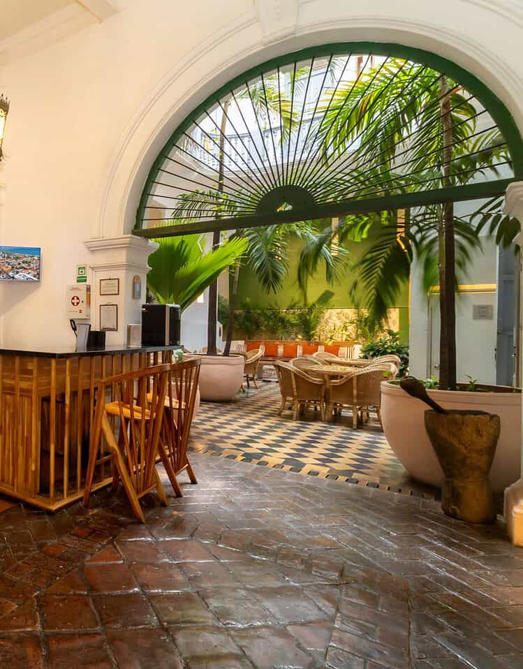 Interior del vestíbulo de un hotel boutique M con escaleras y área de descanso con plantas tropicales.