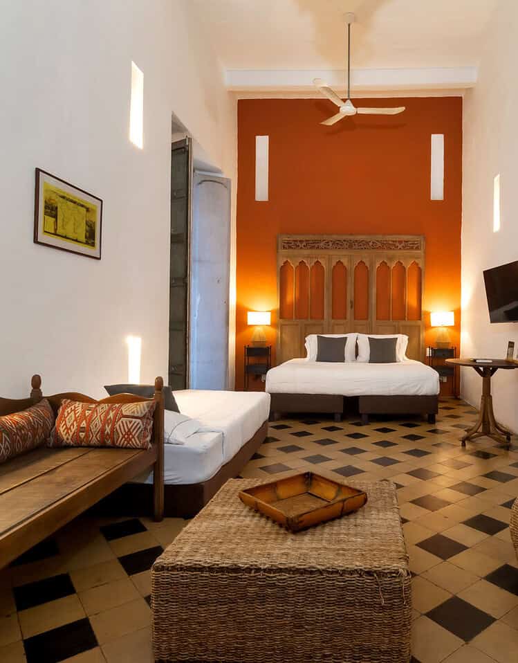Habitación de hotel con cama grande, muebles de madera y decoración colonial en tonos cálidos.