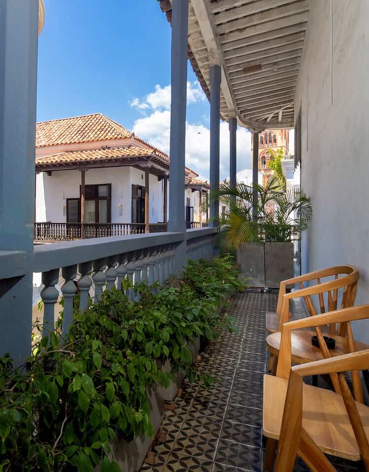 Balcony con vista en un hotel boutique de M, con sillas de madera y plantas verdes, bajo un cielo azul con nubes blancas.