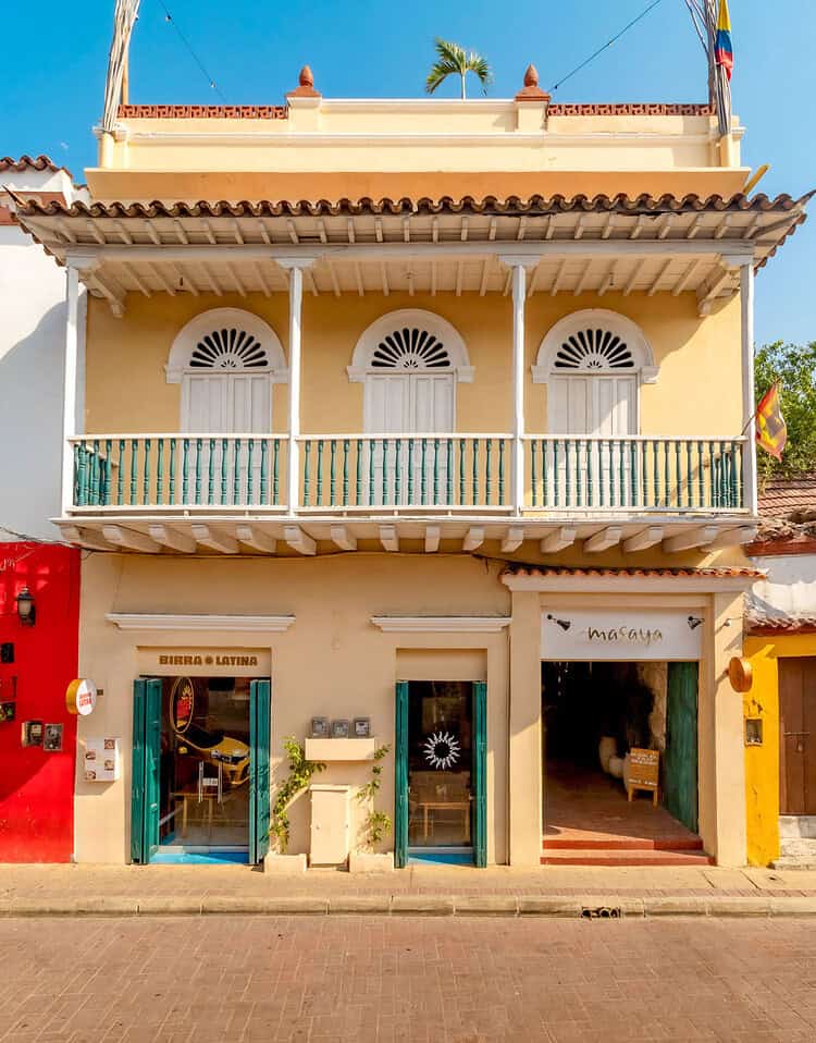 Edificio colonial de dos pisos con balcón y ventanas arqueadas, en un día soleado con cielo azul.