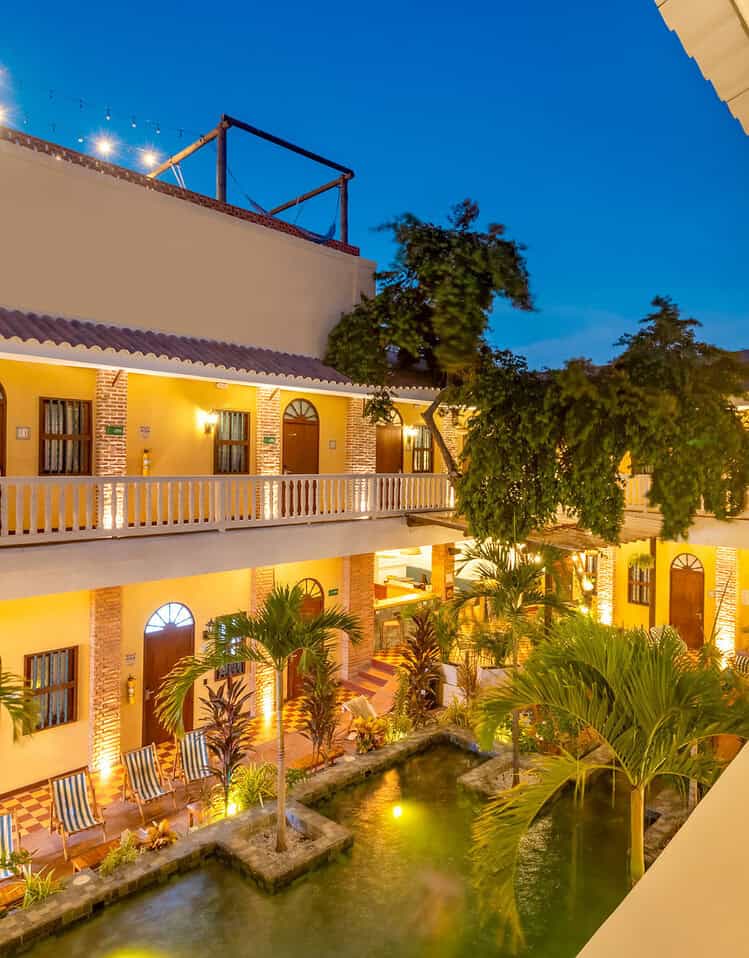 Patio y jardines del hotel M iluminados por la noche, con piscina y vegetación tropical.