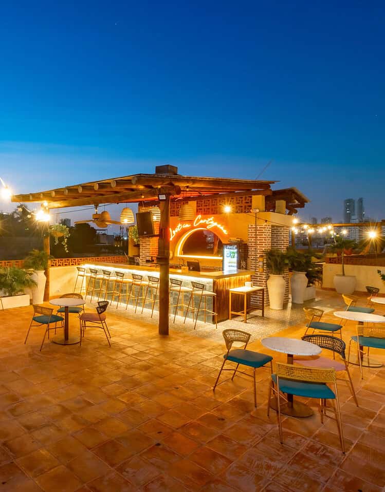Terraza al atardecer en M, con mobiliario y luces decorativas, ideal para relajarse y disfrutar del ambiente urbano.