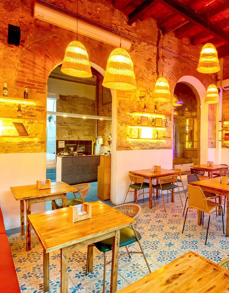 Vista del interior del restaurante M con mesas, sillas y lámparas de mimbre colgantes en un ambiente cálido y acogedor.