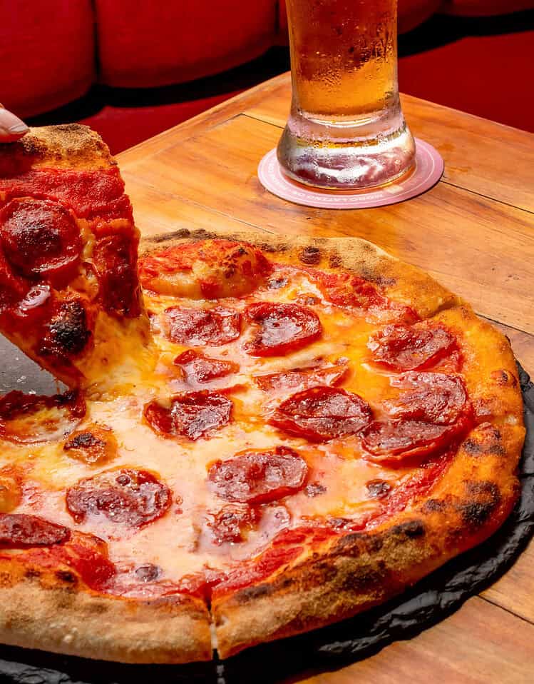 Pizza de pepperoni caliente y crujiente con una cerveza fría en una mesa de madera.