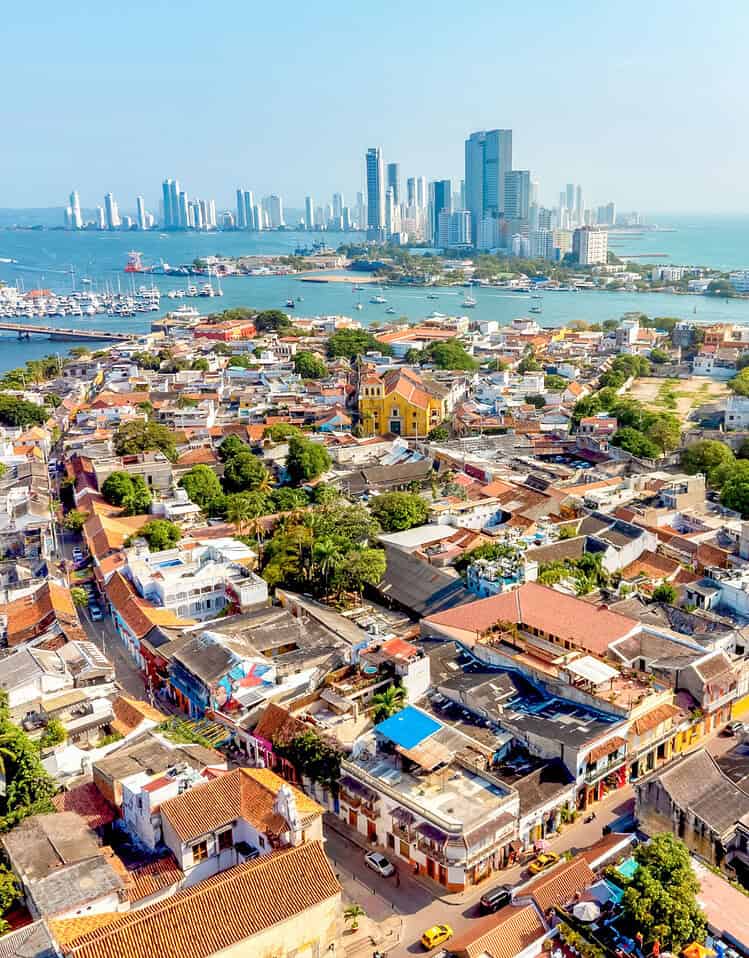 Vista panorámica de la ciudad costera con edificios históricos y modernos, y el mar en el fondo, en un día soleado.