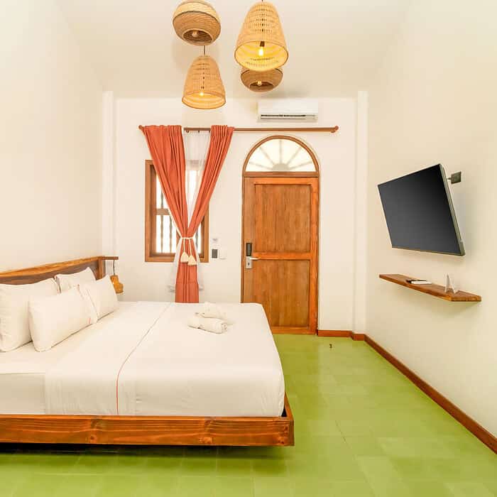 Habitación moderna con cama doble, paredes blancas, cortinas naranjas y suelo verde en M.