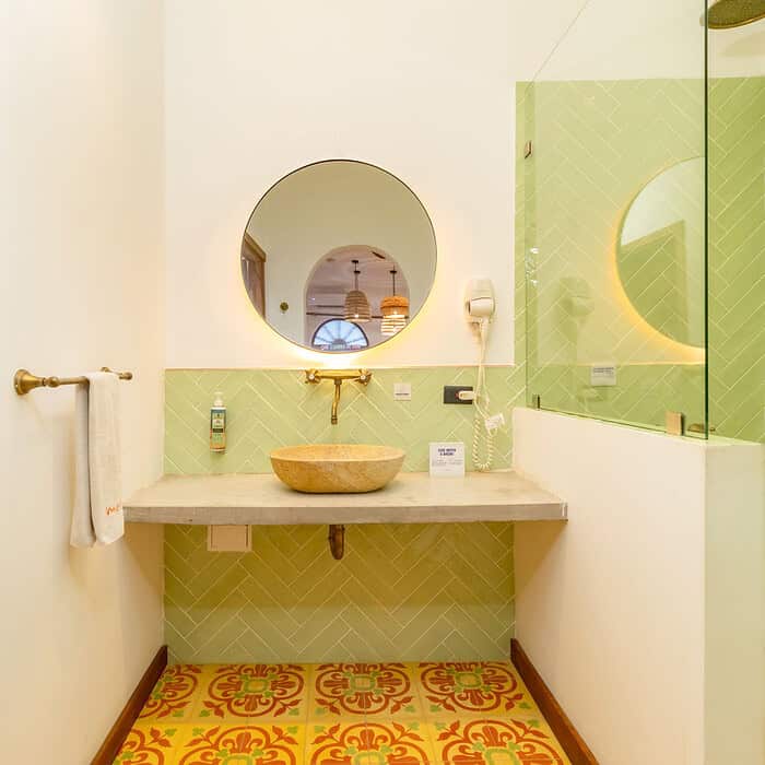 Baño con lavabo de piedra, espejo redondo y paredes verdes en alojamiento M.