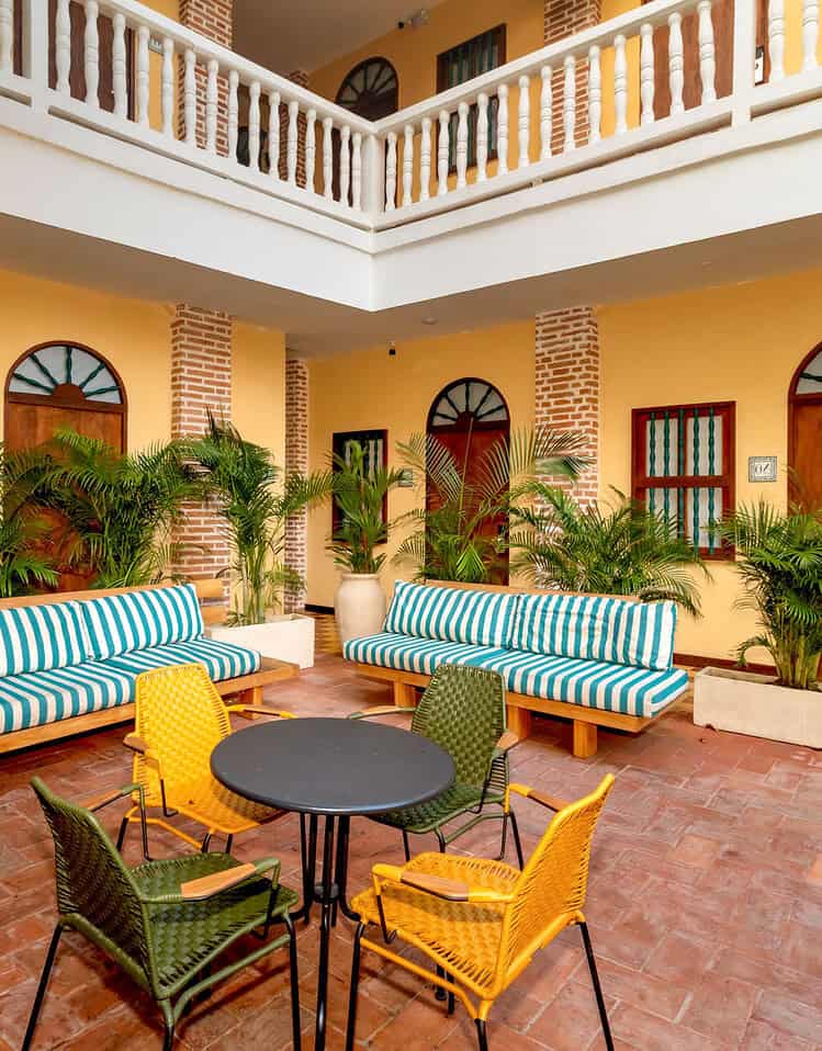 Patio interior de M con muebles de colores y plantas verdes, en un ambiente cálido y acogedor.