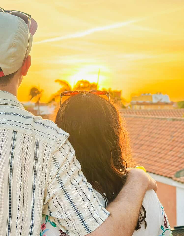 Pareja disfrutando del atardecer en un entorno urbano con tejados rojos y palmeras.